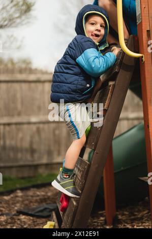 Ragazzo che sale sulla scala del parco giochi mentre si toglie la lingua Foto Stock