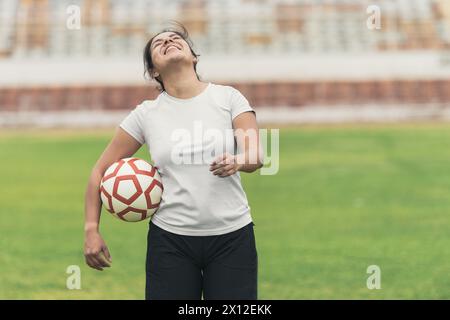 Donna sorridente mentre tiene in mano una palla da calcio sul campo Foto Stock