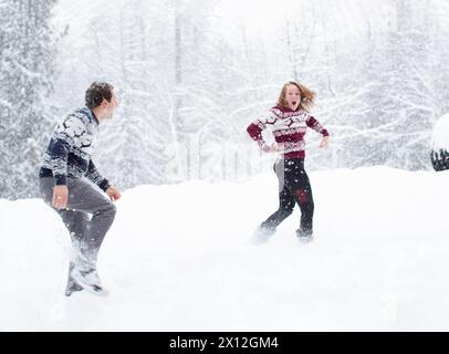 Lotta con la palla di neve tra coppia nei maglioni natalizi Foto Stock