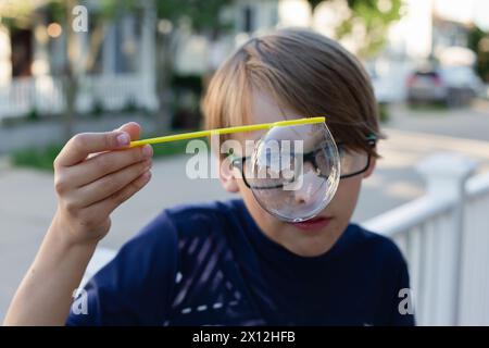 Ragazzo biondo con gli occhiali che soffiano bolle Foto Stock