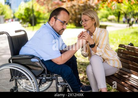 L'uomo in sedia a rotelle sta trascorrendo del tempo con sua madre nel parco. Foto Stock