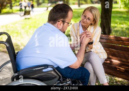 L'uomo in sedia a rotelle sta trascorrendo del tempo con sua madre nel parco. Foto Stock