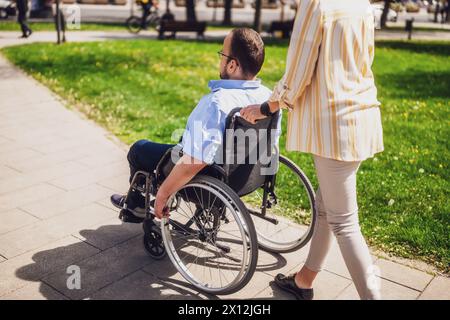 L'uomo in sedia a rotelle sta trascorrendo del tempo con sua madre nel parco. Stanno godendo la giornata di sole insieme. Foto Stock