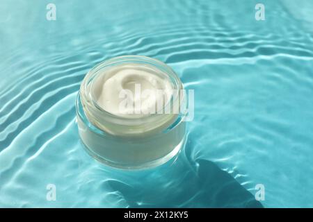 Vaso con crema idratante in acqua su sfondo azzurro Foto Stock