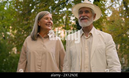Felici nonni caucasici pensionati coppia pensionati donna sorridente uomo passeggiare insieme parlare pensione all'aperto parco naturale cittadino. Un anziano gioioso Foto Stock