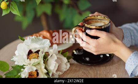 Primo piano di mani femminili che tengono una tazza di caffè nera Foto Stock