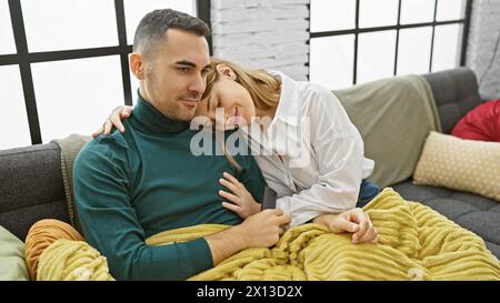 Una coppia amorevole si coccola su un divano in un accogliente soggiorno, ritraendo un caldo legame emotivo. Foto Stock