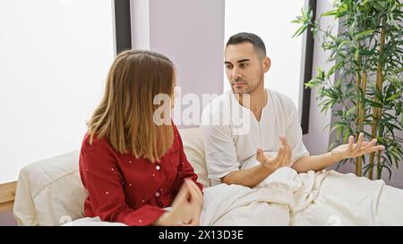 Un uomo e una donna conversano seriamente in una camera da letto luminosa, raffigurando un momento di dinamica relazionale. Foto Stock