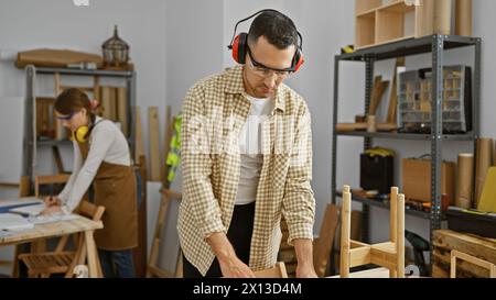 Un team di carpentieri uomo e donna lavora insieme in un laboratorio di lavorazione del legno ben attrezzato, concentrandosi sulla produzione di mobili. Foto Stock