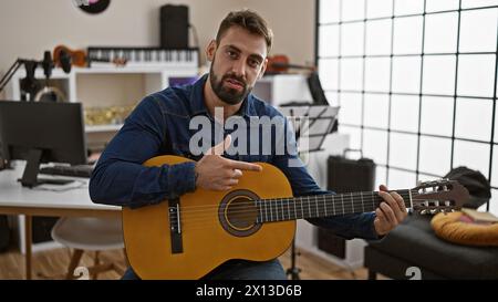Giovane ispanico che suona accordi classici sulla sua chitarra, coinvolto in una conversazione vivace in uno studio di musica al chiuso Foto Stock