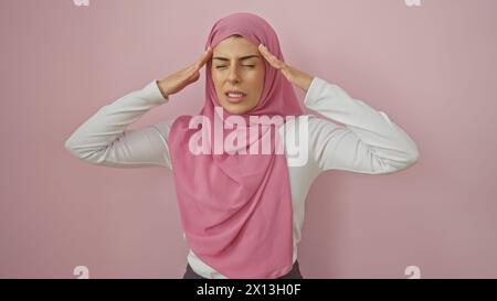 Una giovane donna in un hijab rosa che esprime mal di testa su uno sfondo rosa isolato Foto Stock