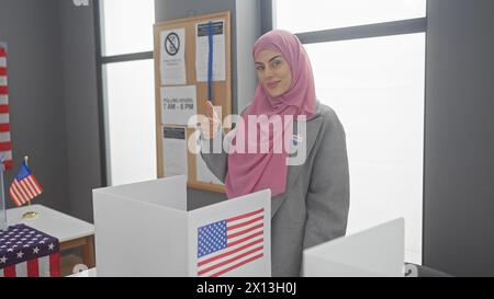 Una giovane donna con un hijab regala un pollice in una cabina elettorale con bandiere americane. Foto Stock