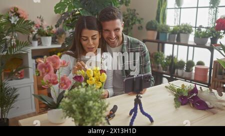 Una donna e un uomo che organizzano fiori mentre registrano un tutorial in un negozio di fiori al coperto pieno di flora. Foto Stock