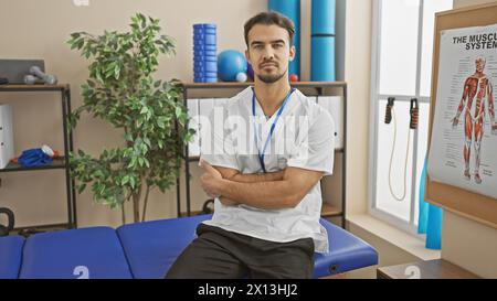 Bellissimo terapeuta ispanico maschile con le braccia in piedi della barba incrociate in una clinica di riabilitazione ben attrezzata. Foto Stock