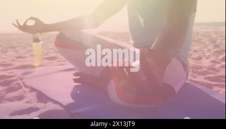 Immagine di macchie di luce su un uomo afroamericano che meditava sulla spiaggia Foto Stock