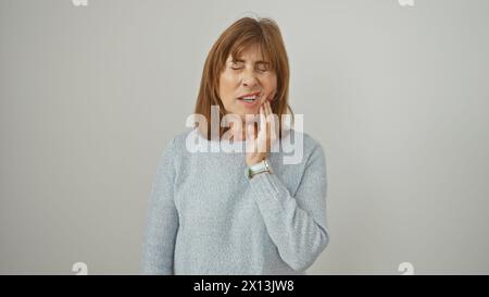 Una donna di mezza età soffre di mal di denti, tenendo la guancia su uno sfondo bianco. Foto Stock