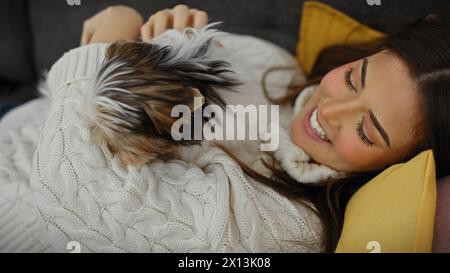 Sorridente giovane donna che si accoccolava con il suo terrier yorkshire biewer su un divano a casa. Foto Stock