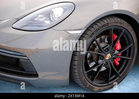 Dettaglio di una ruota nera satinata con pinza rossa e faro di una Porsche Cayman. Foto Stock