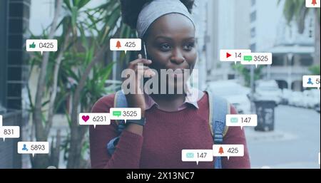 Immagine di più icone dei social media su una donna afroamericana che parla all'aperto su smartphone Foto Stock