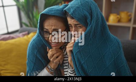 Due donne che condividono un momento emotivo sotto una coperta blu su un divano a casa Foto Stock