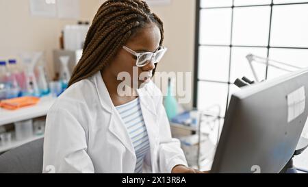 Una donna afroamericana concentrata con trecce che lavora in un laboratorio, al chiuso. Foto Stock