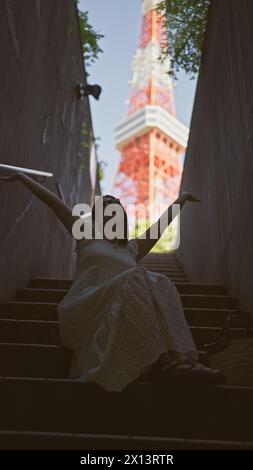 Bellissima donna ispanica con occhiali appollaiati sulle scale, un ritratto della modernità urbana nel famoso punto della torre di tokyo Foto Stock