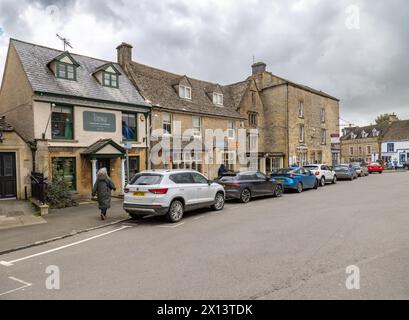 Un'affascinante Stow sulla Wold Street fiancheggiata da negozi di pietra del Cotswold e auto parcheggiate, catturando l'essenza della vita dei villaggi inglesi. Foto Stock
