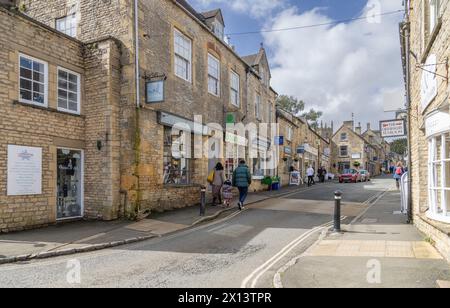 I turisti e gli amanti dello shopping passeggiano lungo una strada costeggiata da negozi di pietra del Cotswold color miele a Stow on the Wold. La popolare destinazione delle Cotswolds. Foto Stock