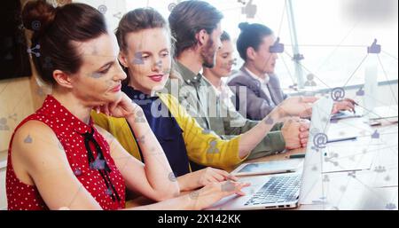 Immagine di icone di computer collegate a linee su diversi colleghi che utilizzano la tecnologia sulla scrivania Foto Stock