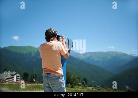 ragazzo che osserva il panorama delle montagne attraverso un binocolo fisso Foto Stock