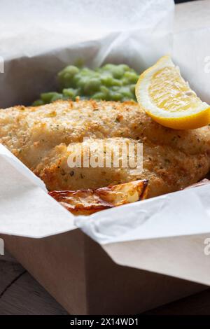 Takeaway di fish and chips con piselli di muschio e limone. Scatola di cartone da asporto ecologica, biodegradabile e priva di plastica. Foto Stock