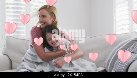 Immagine di cuori sopra la felice donna caucasica e sua figlia seduta sul divano, abbracciando Foto Stock