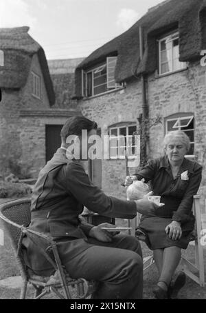 TRUPPE STATUNITENSI IN UN VILLAGGIO INGLESE: LA VITA DI TUTTI I GIORNI CON GLI AMERICANI A BURTON BRADSTOCK, DORSET, INGHILTERRA, Regno Unito, 1944 - la signora Howarth, moglie del maestro del villaggio, versa il tè per il sergente Harold D Kregar nel giardino della sua casa a Burton Bradstock nel Dorset. Il sergente Kregar è di Cheyenne Wells, Colorado, e ha vinto la Legion of Merit in Islanda Foto Stock