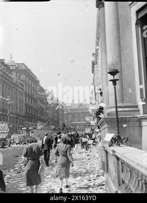 LE CELEBRAZIONI DEL VJ DAY, 15 AGOSTO 1945 - i civili camminano tra le pile di carta strappata che sono state gettate, in stile "nastro adesivo", dalle vetrine degli uffici, in Lower Regent Street, Londra, per celebrare la firma della pace con il Giappone, 15 agosto 1945.si può vedere altra carta sventolare giù sul marciapiede e sulla strada: molti veicoli sembrano essersi fermati. Sembra che questa foto sia stata scattata in Lower Regent Street, guardando indietro verso Piccadilly Circus. Al centro della strada (a sinistra della fotografia), è possibile vedere un riparo in superficie di mattoni Foto Stock