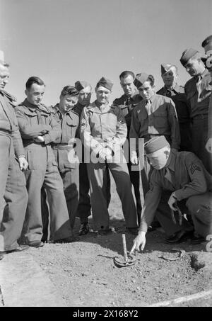 TRUPPE STATUNITENSI IN UN VILLAGGIO INGLESE: LA VITA QUOTIDIANA CON GLI AMERICANI A BURTON BRADSTOCK, DORSET, INGHILTERRA, Regno Unito, 1944 - al sole al campo americano di Burton Bradstock, il sergente James F Hokanson (del 1062 McLemore, Memphis, Tennessee) spiega come giocare il gioco dei "ferri di cavallo" ai soldati di un'unità di ricerca britannica stanziata nelle vicinanze. La didascalia originale afferma che "i due eserciti si sono presto fatti amici, visitano i campi dell'altro, mangiano insieme, giocano" Foto Stock