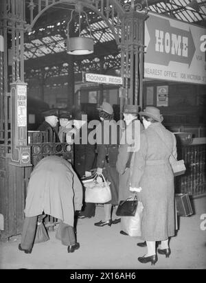 THE CARTERS IN WARTIME: EVERYDAY LIFE FOR A BRITISH FAMILY ON THE HOME FRONT, ENGLAND, C 1940 - la signora Carter fa la fila per mostrare il suo biglietto al cancello di una piattaforma, Victoria Station, Londra, mentre si recava a visitare i suoi due figli, che sono stati evacuati a Hayward's Heath, nel Sussex. Notare la custodia della maschera antigas trasportata dalla donna sul retro della coda Foto Stock