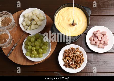 Fonduta con gustosi formaggi fusi, forchette, vino e diversi spuntini su un tavolo di legno, piatto Foto Stock