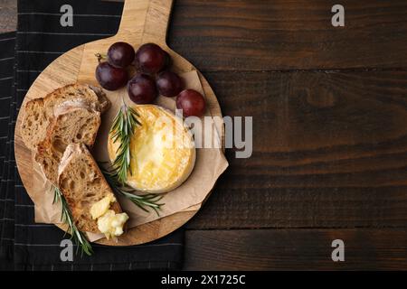 Gustoso camembert al forno, pezzi di pane, uva e rosmarino su un tavolo di legno, vista dall'alto. Spazio per il testo Foto Stock