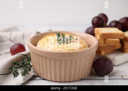 Gustoso camembert al forno in ciotola, timo, uva e crostini su tavola di legno, primo piano Foto Stock