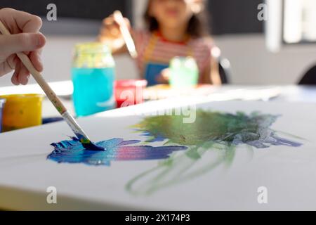 Nella classe d'arte scolastica, ragazza birazziale e ragazza caucasica, entrambe giovani, dipingono insieme Foto Stock