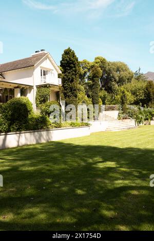 Il lussureggiante prato verde conduce a una grande casa bianca con alberi a casa Foto Stock