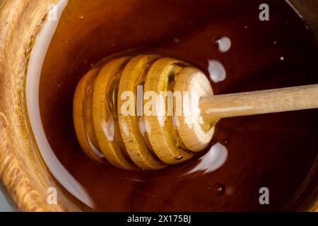 miele d'api liquido in una ciotola di legno, vero miele d'api proveniente da fiori di polline in una ciotola di legno sul tavolo Foto Stock