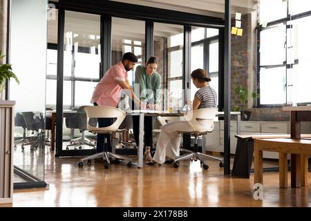 La signora asiatica di mezza età parla con un giovane uomo asiatico e colleghi di donne caucasiche in un business moderno Foto Stock