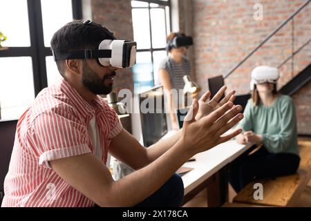 Un team eterogeneo sta esplorando la realtà virtuale indossando cuffie e auricolari in un moderno ufficio aziendale Foto Stock