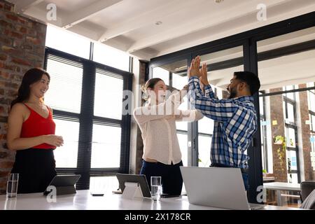 Un team diversificato che festeggia in un moderno ufficio aziendale, con laptop sul tavolo Foto Stock