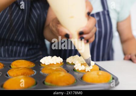 La nonna asiatica e la nipote adolescente birazziale stanno decorando i cupcake a casa Foto Stock