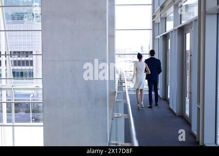 Colleghi birazziali che camminano lungo il corridoio dell'ufficio Foto Stock