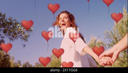 Immagine di palloncini rossi a cuore che fluttuano sopra la coppia in amore tenendosi per mano in estate Foto Stock