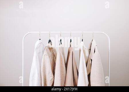 Capi essenziali per il guardaroba nei colori bianco e beige, chiusura elegante da donna sul rack Foto Stock