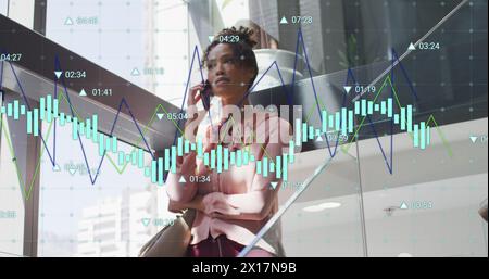 Immagine di più grafici e numeri che cambiano rispetto a una donna birazziale che parla al cellulare Foto Stock